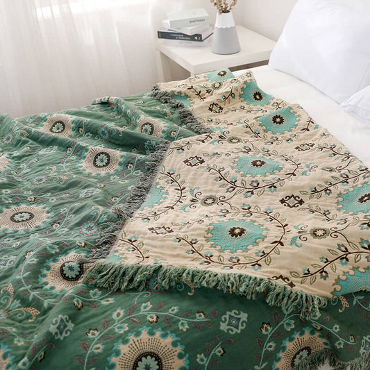Green and beige floral throw blanket with fringe on a white bed in a bright, cozy bedroom
