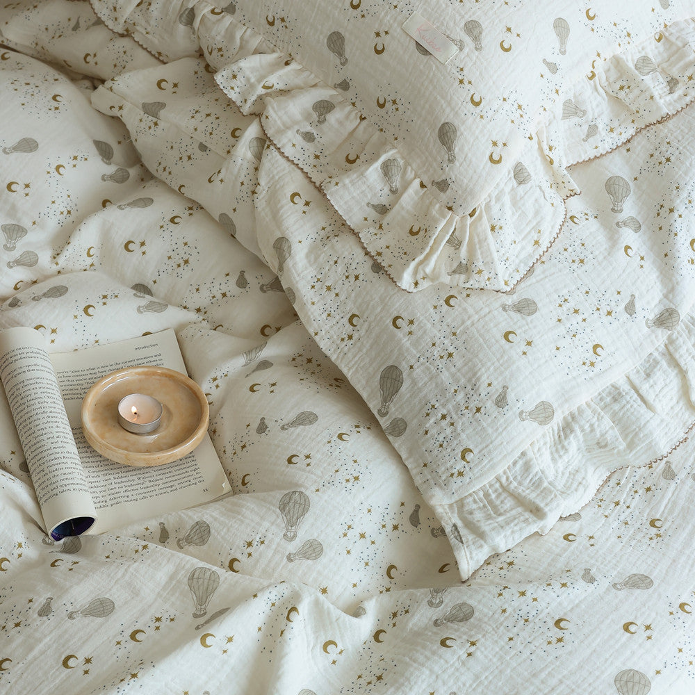 Soft cotton gauze bedding with a hot air balloon print and ruffled edges, styled with a book and candle.
