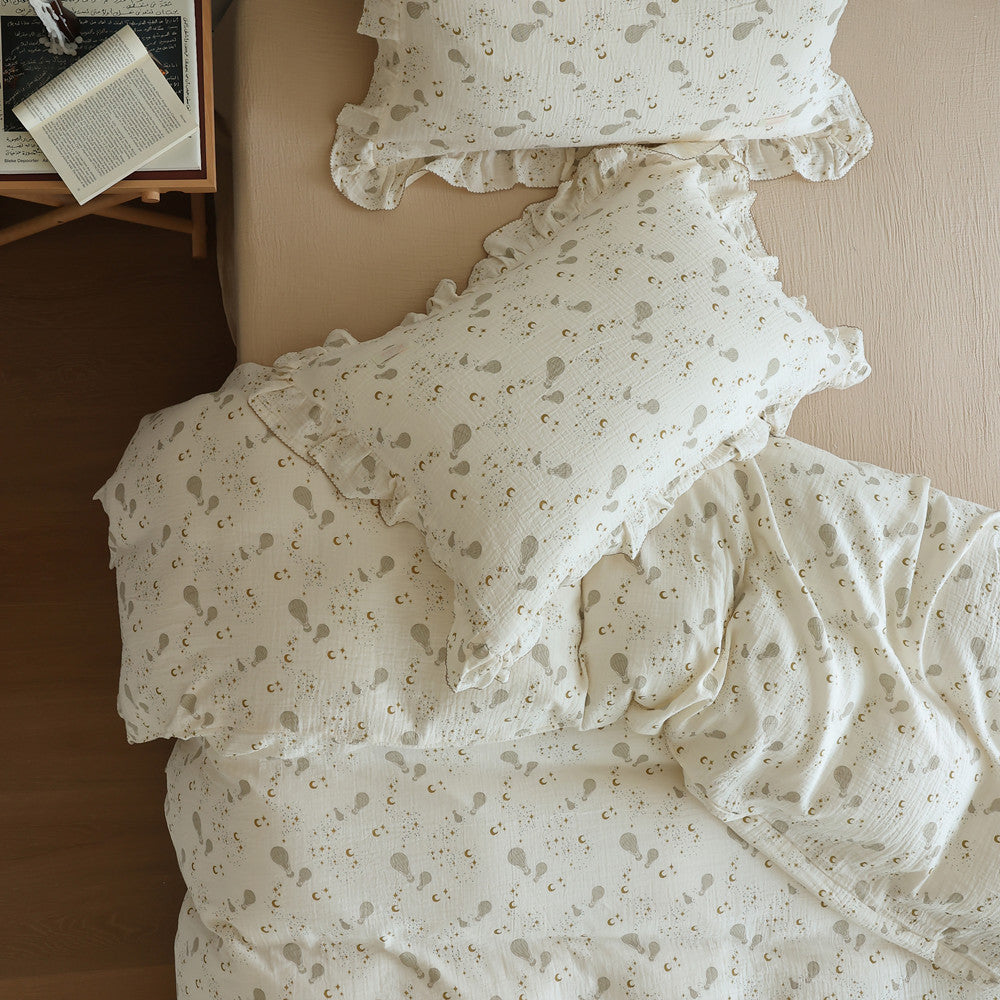 Overhead view of a bed with cotton muslin bedding featuring a hot air balloon print and ruffled pillow shams.