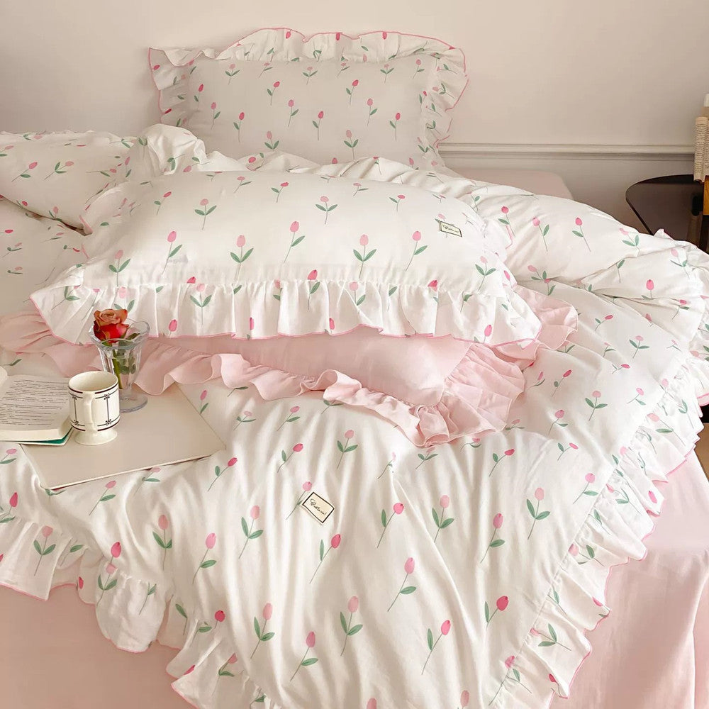 A bedding set with a floral pattern consisting of pink tulips, with white sheets and pink ruffle edges, displayed on a bed.