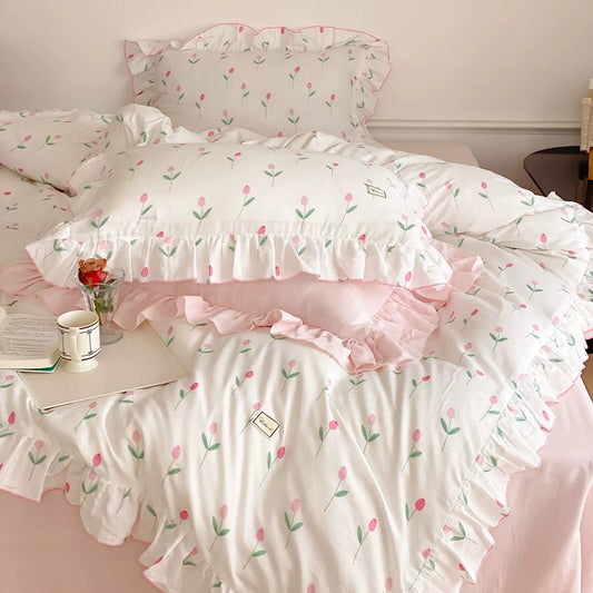 A bedding set with a floral pattern consisting of pink tulips, with white sheets and pink ruffle edges, displayed on a bed.