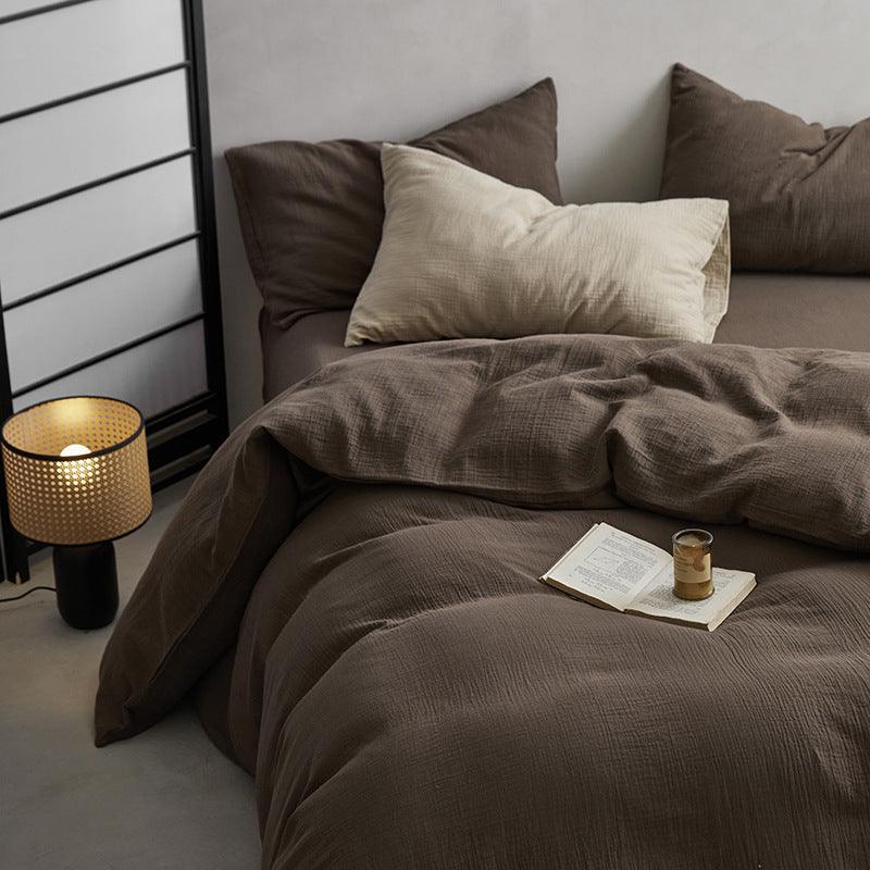 Bed with brown bedding and pillows, nightstand with lamp, and a book and mug on the bed.