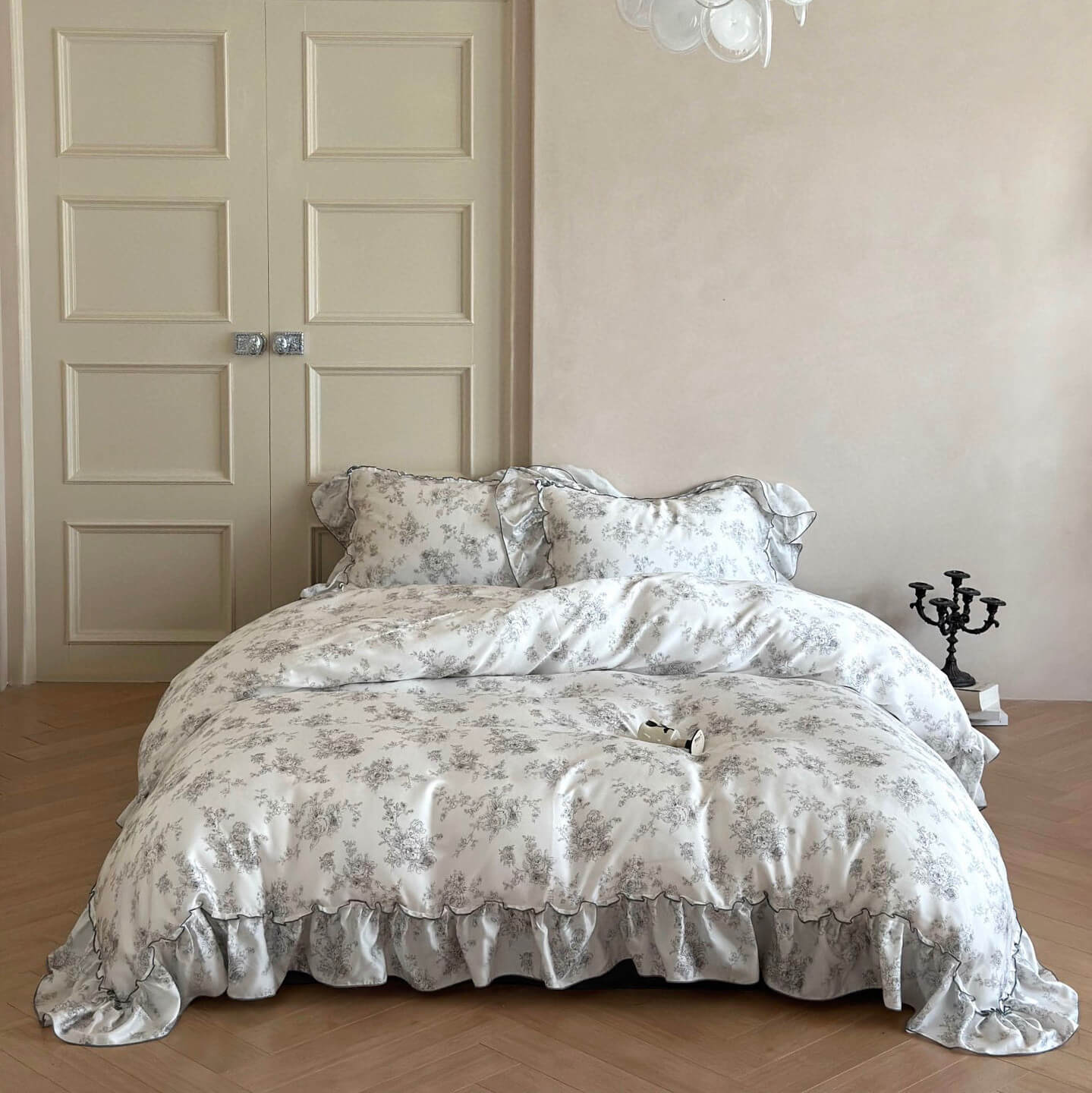 Full view of a French style floral ruffle bedding set on a bed in a light, elegant room with white doors.