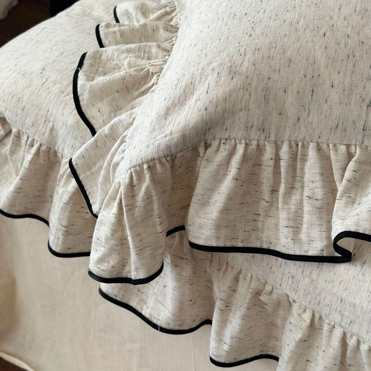 Close-up of white cotton ruffled bedding detail, showing the textured fabric and black trim on the ruffle duvet set and pillow sham.