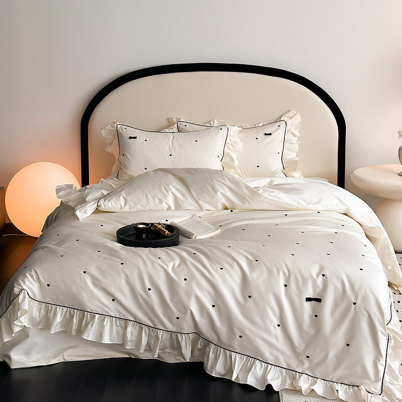 Ivory White Ruffled Bedding Set, full view with delicate heart embroidery and black piping details for a modern look.