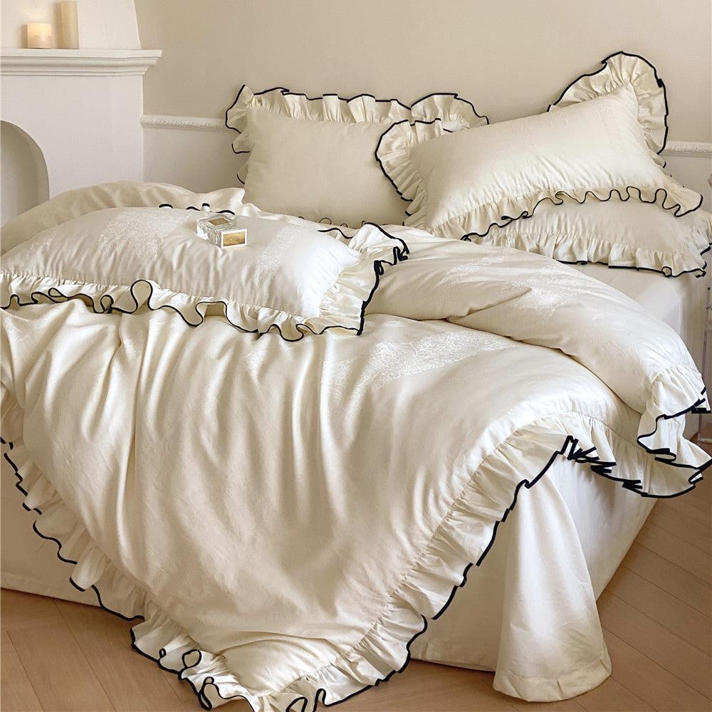 Full bed view of the satin ruffle bedding set in cream white with black trim, highlighting its elegance and layered pillows in a bright room.