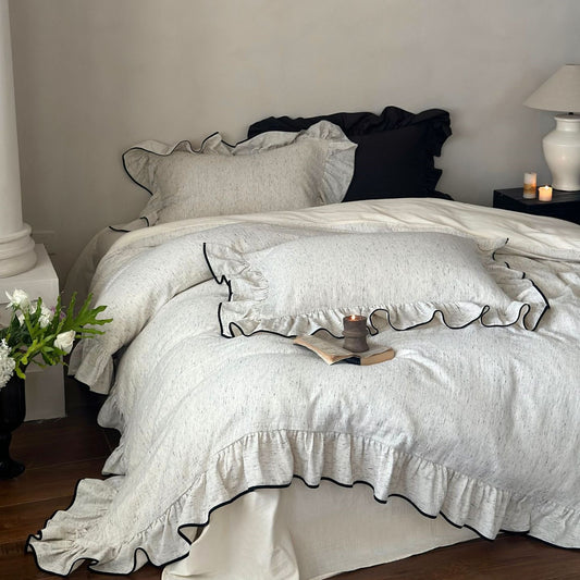 A bed with chic ruffled bedding, including a duvet cover, flat sheet, and pillowcases, in a neutral color, displayed in a bedroom setting.