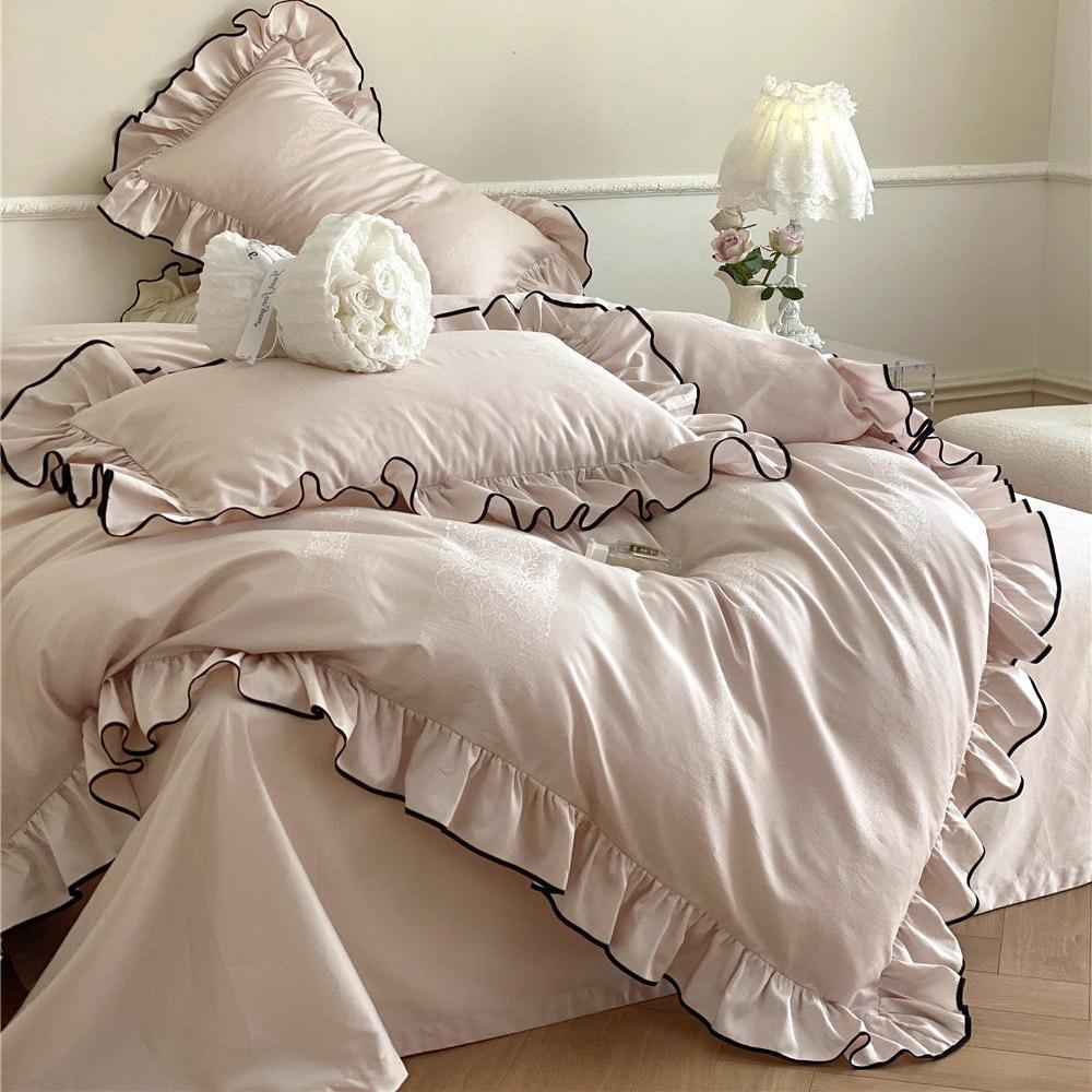 Full bed view of the silky frill bedding set in light pink with black piping, featuring layered pillows and a bouquet of white roses.
