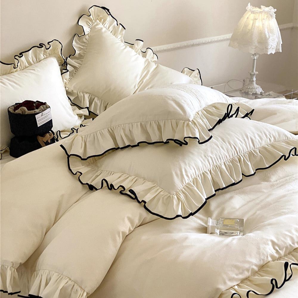 Close-up of silky ruffled bedding set in cream white with black trim, showing satin sateen fabric texture and decorative pillows.