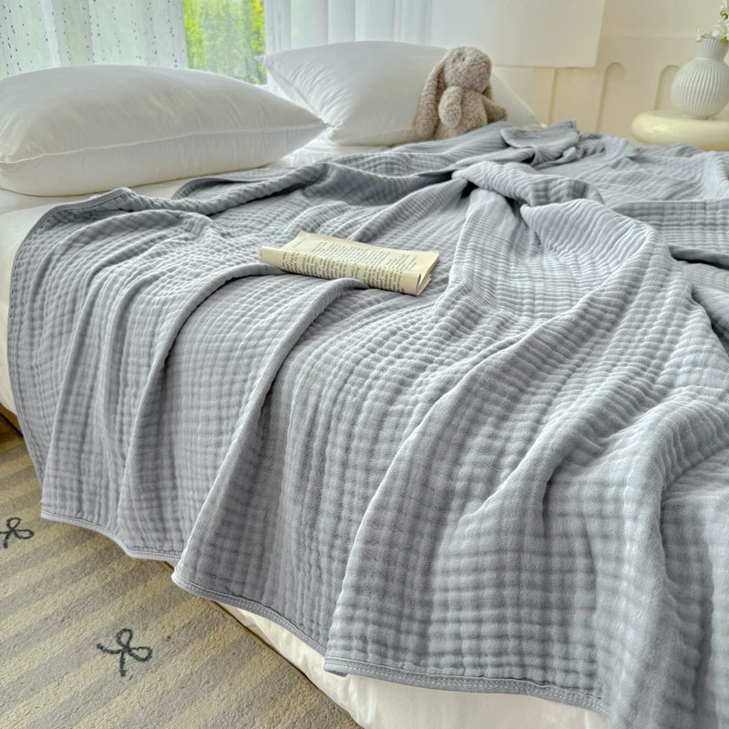 Light grey 6-layer cotton gauze blanket covering a bed, showing the cozy, pleated texture.