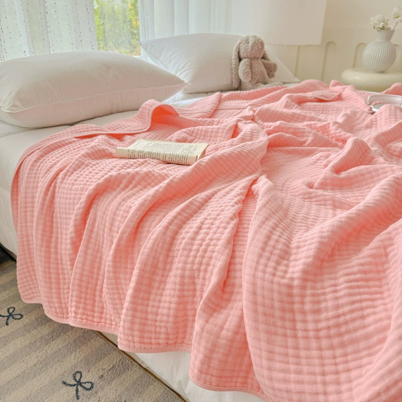 Soft blush pink 6-layer cotton gauze blanket draped on a bed, perfect as a lightweight throw.
