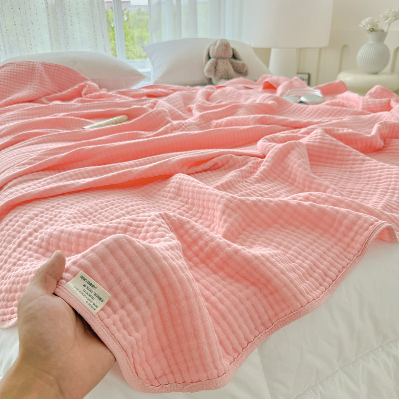 Hand holding up a blush pink 6-layer cotton gauze blanket, highlighting the lightweight and soft feel.