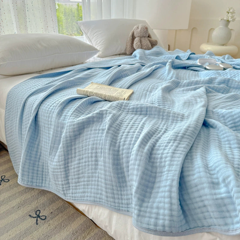 Soft sky blue 6-layer cotton gauze blanket draped over a bed in a bright room.