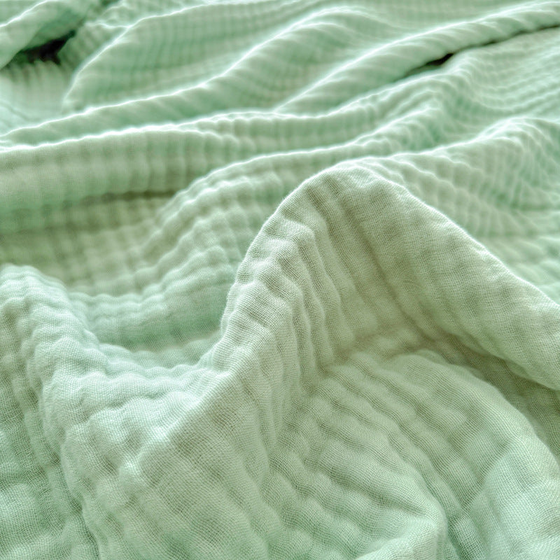 Close-up view of a sage green 6-layer cotton gauze blanket, highlighting the breathable, crinkled texture.