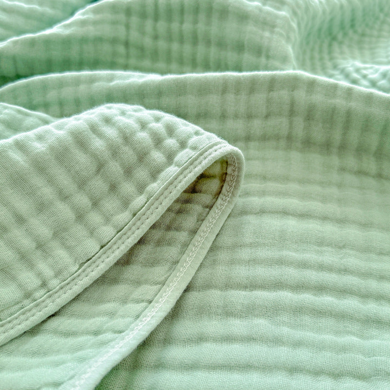Detailed close-up of the stitching and folded edge on a soft sage green 6-layer cotton gauze blanket.