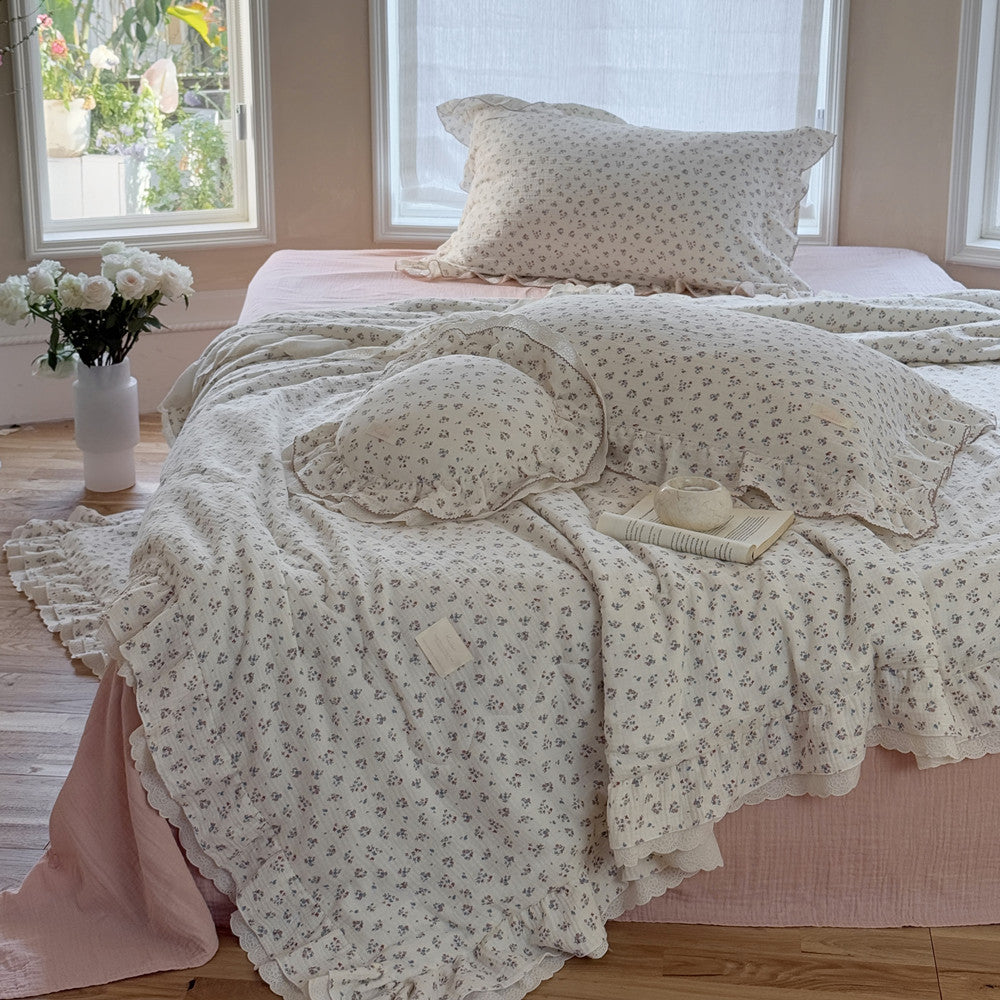 Lightweight cotton comforter with floral design and round ruffle pillow, styled in a cozy space