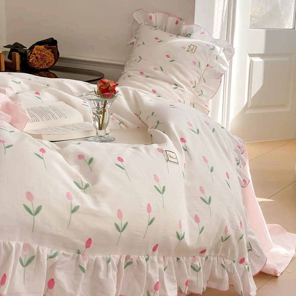 Bedside shot of the Pink Tulip Bedding Set, showcasing the cotton muslin floral print, ruffles, open book, and single rose decoration.