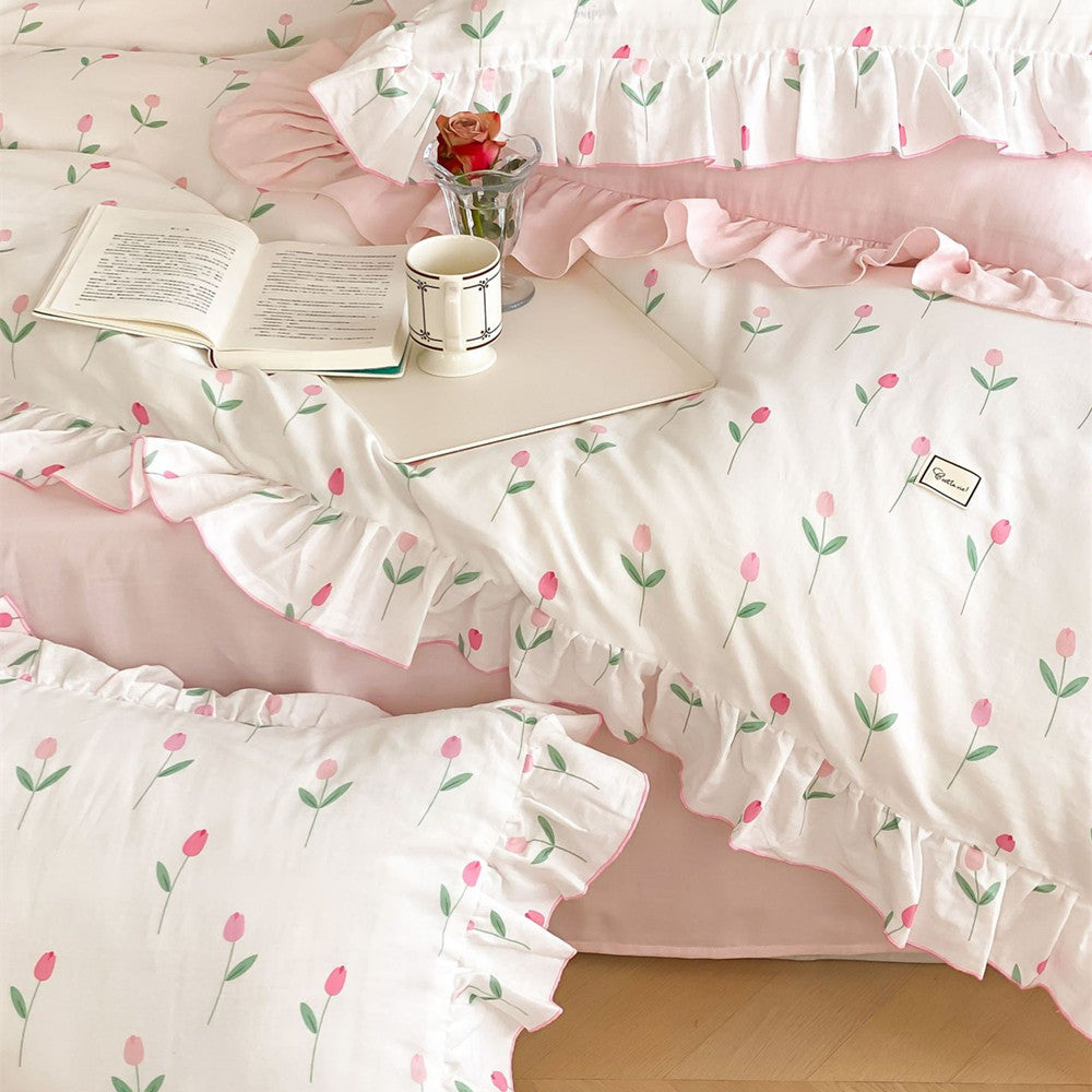 Close-up of Pink Tulip Bedding Set in Soft Cotton Muslin, showing the floral pattern, ruffled edge, open book, and coffee mug detail.
