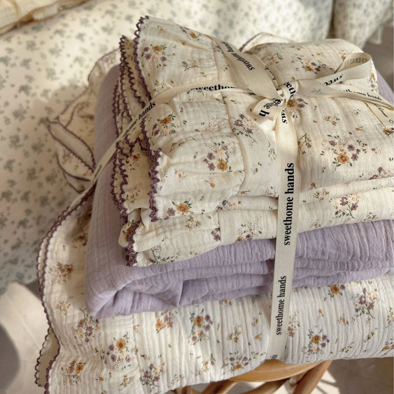 Stacked cotton muslin duvet set with yellow floral print and solid purple layer, tied with ribbon.