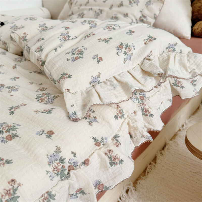 A close-up side-angle shot of a floral muslin gauze duvet cover and a matching pillow on a bed, showcasing the delicate floral pattern and ruffled edges.
