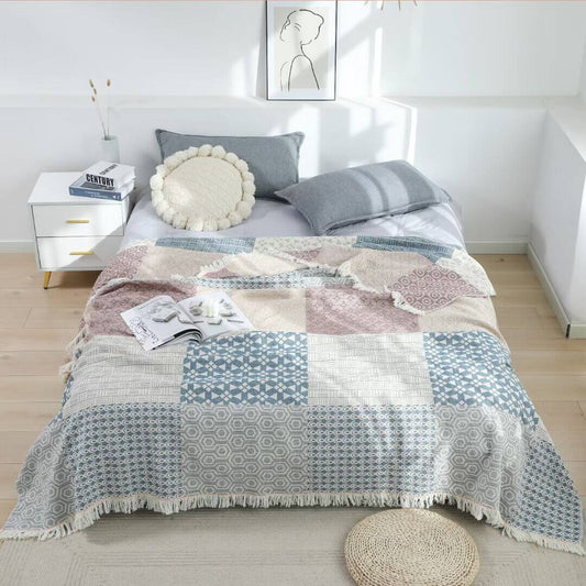 Full view of a rectangular 100% cotton throw blanket spread on a bed, displaying a modern block pattern of circles, hexagons, and triangles.