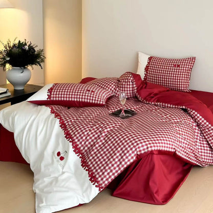 Cozy bedroom scene with red and white gingham cotton bedding set featuring cherry embroidery, white pillow, and bedside table with vase and lamp