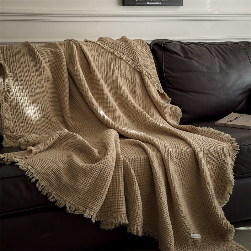 Beige 6-layer cotton muslin throw blanket with fringe on dark leather sofa in cozy living room