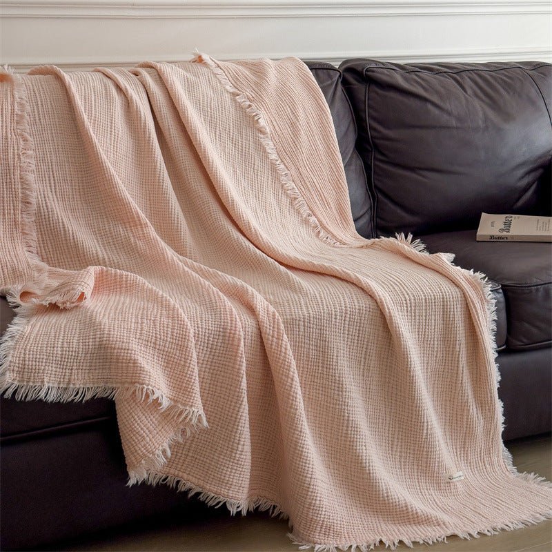 Soft peach 6-layer cotton muslin throw blanket with fringed edges draped on dark sofa