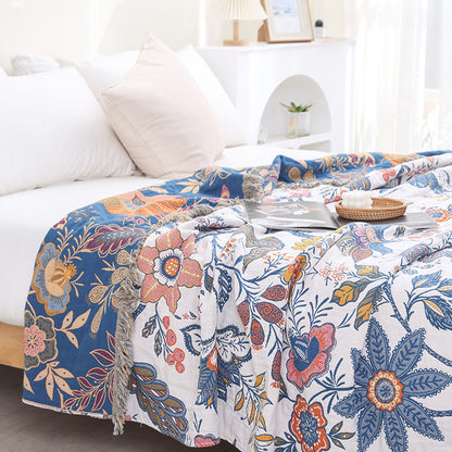 Reversible autumn botanical jacquard cotton throw blanket draped on a bed, showing the navy blue underside and cream floral pattern with fringed edges.