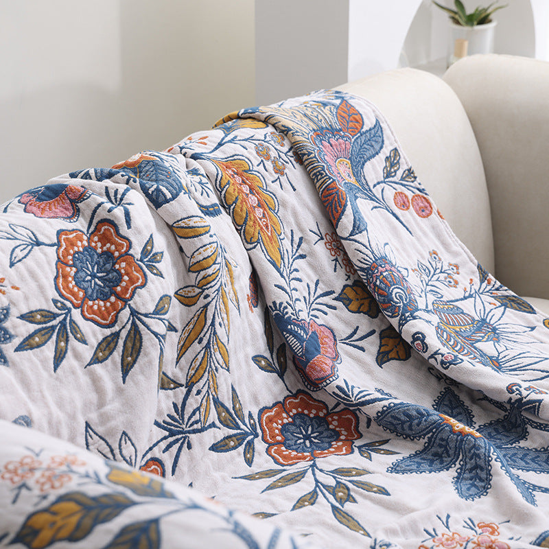 Close-up view of the soft folds of a botanical jacquard cotton blanket, detailing the large orange flower motifs and blue leafy patterns.