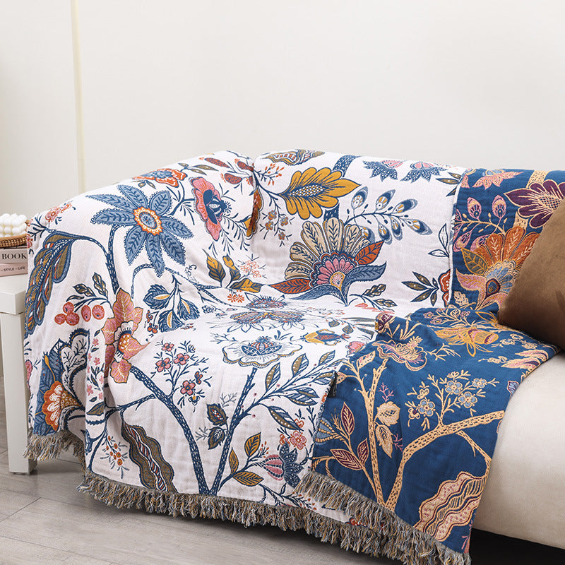 Large autumn botanical cotton throw blanket covering a sofa, featuring a vintage floral print in blue and orange with decorative tassel trim.