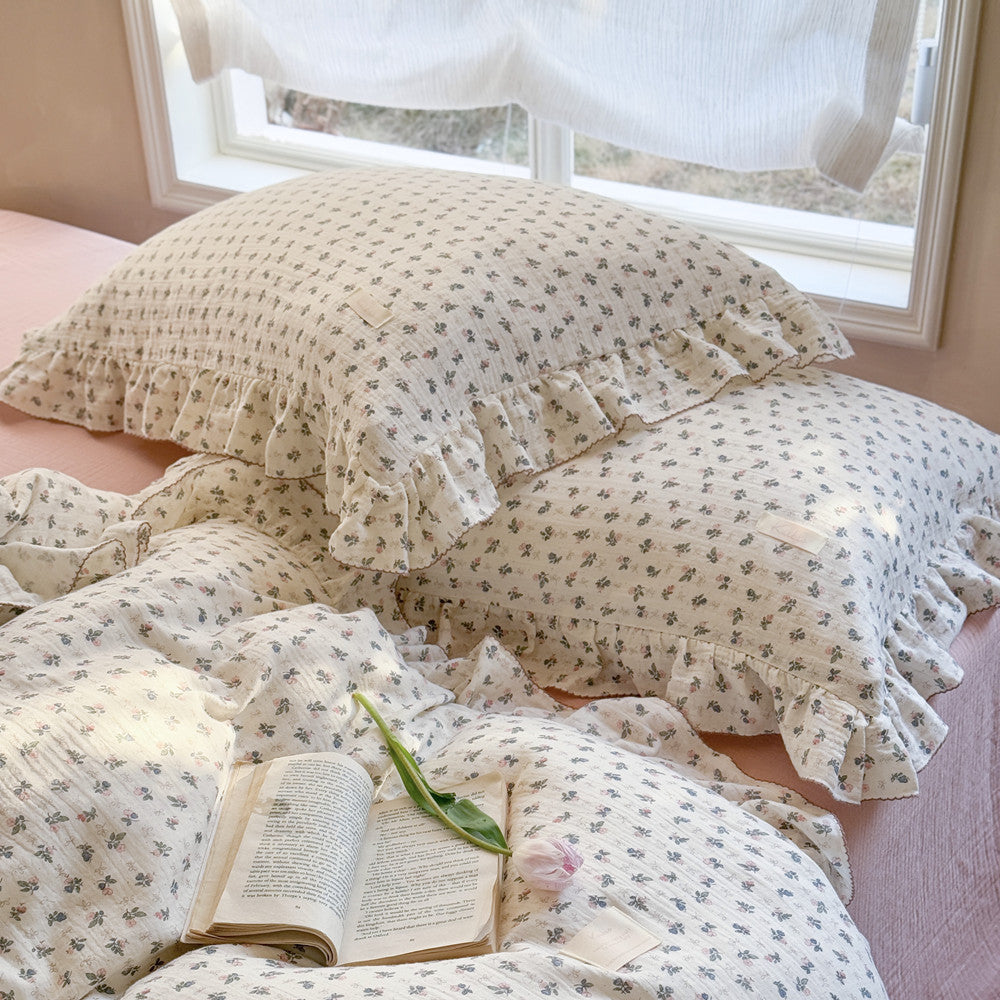 Close-up of two stacked Ruffled Cotton Gauze Pillow Shams and the matching Bellflower Floral Duvet Cover on a pink sheet, highlighting the muslin fabric texture and romantic cottagecore style.
