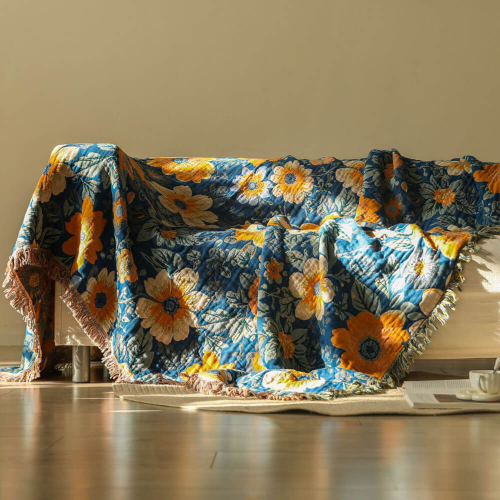Blue daisy floral cotton throw blanket with fringe draped over a sofa