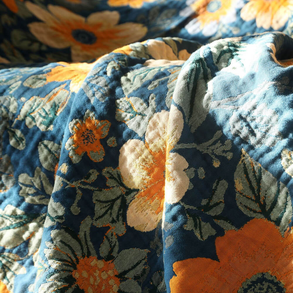 Close-up of blue daisy floral cotton throw blanket with orange and cream flowers