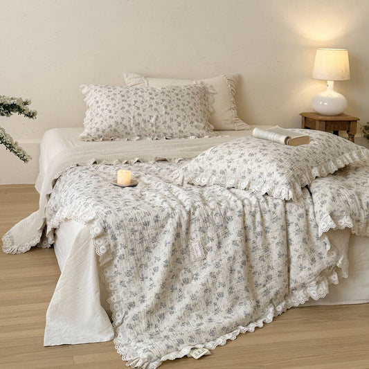 Blue rose cotton comforter with white ruffled lace trim styled on an ivory cottage bed