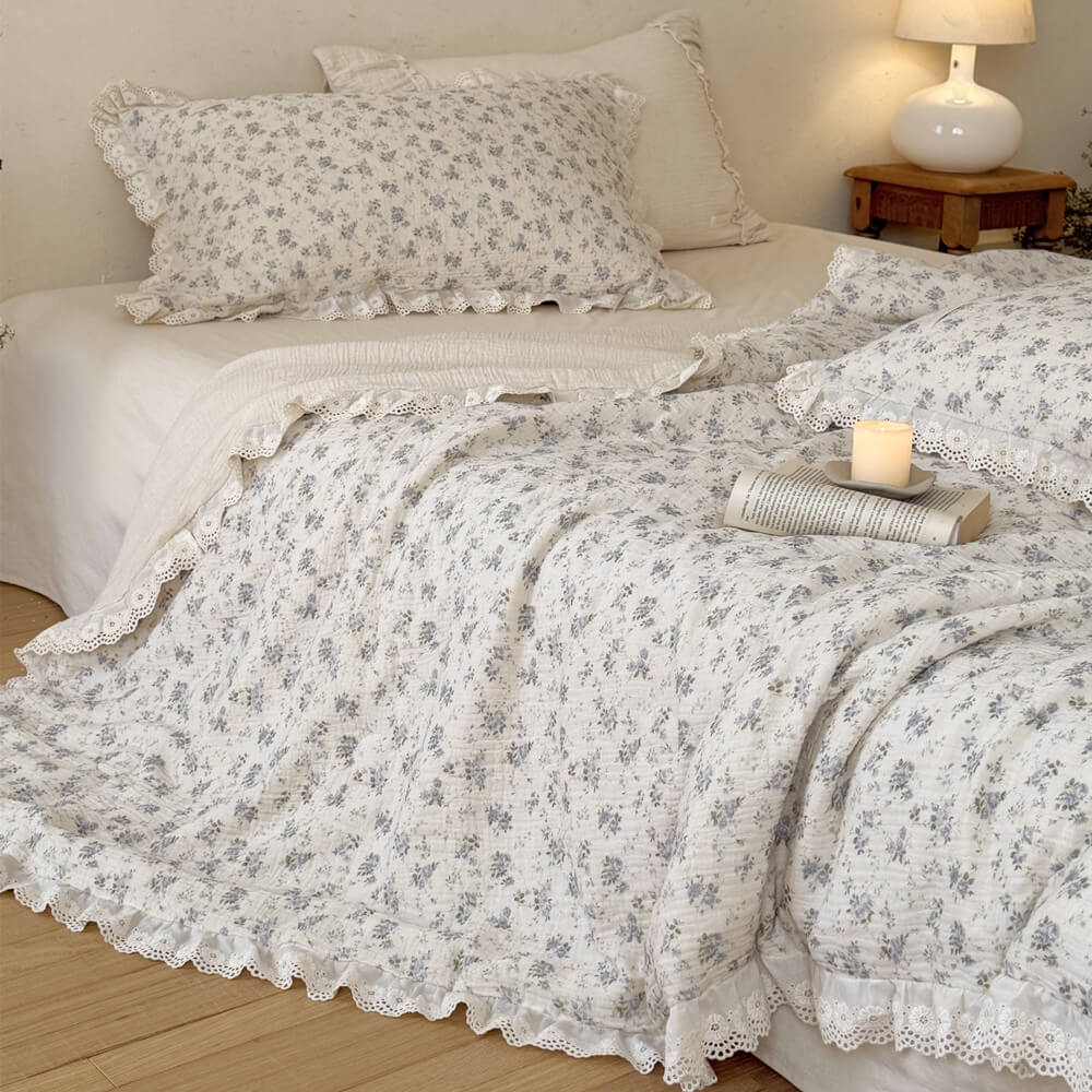 Blue rose cotton comforter with ruffled lace trim styled with candle and open book