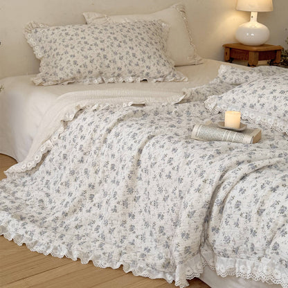 Blue rose cotton comforter with ruffled lace trim styled with candle and open book