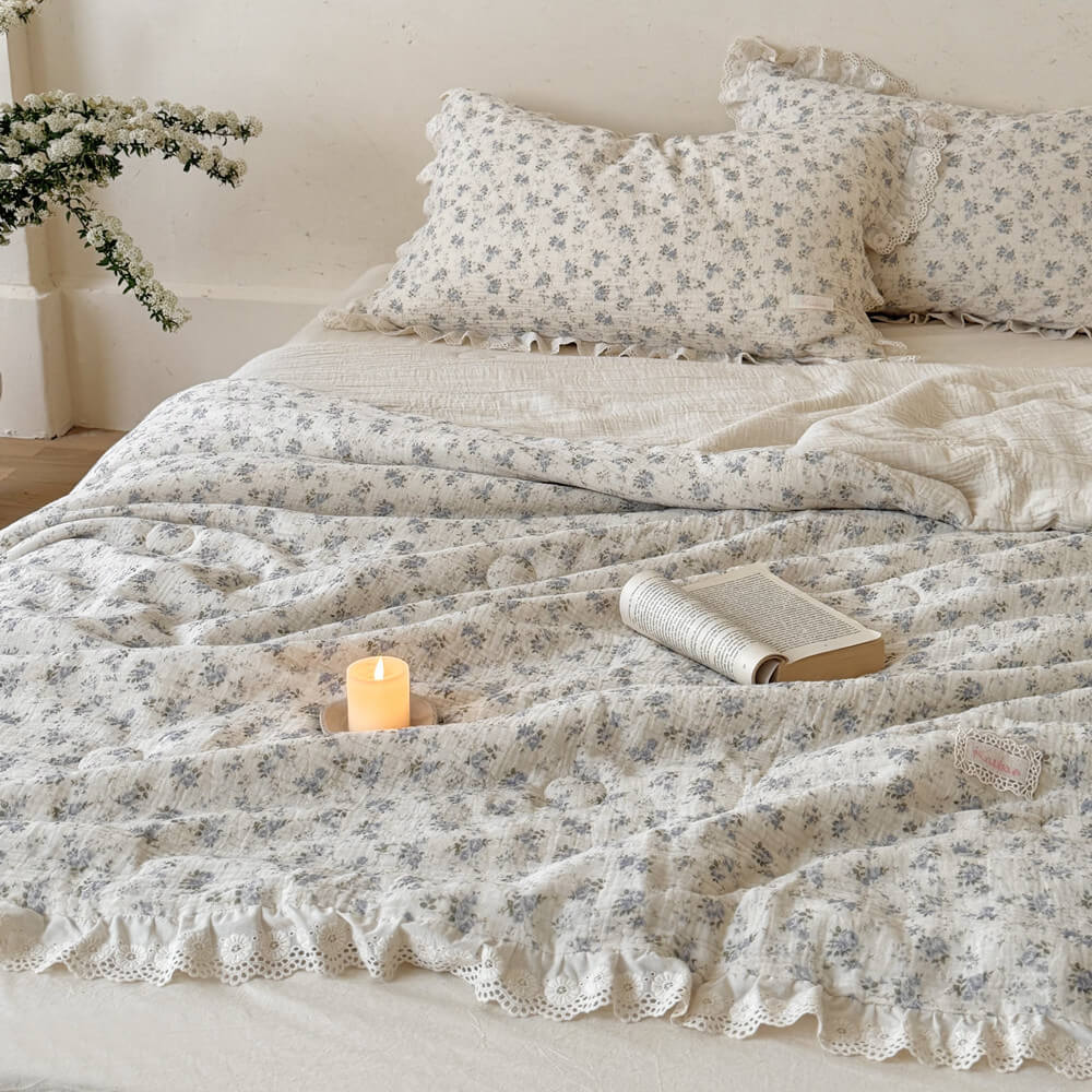 Blue rose comforter and ruffled pillows layered on an ivory bed with candle styling