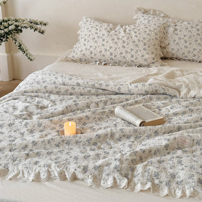 Blue rose comforter and ruffled pillows layered on an ivory bed with candle styling