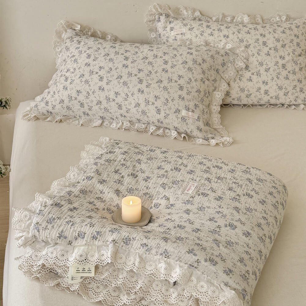 Folded blue rose comforter showing white lace trim, soft texture, and matching styled pillows