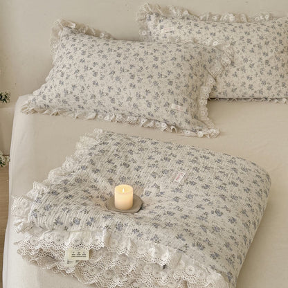Folded blue rose comforter showing white lace trim, soft texture, and matching styled pillows