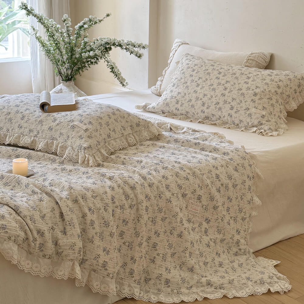 Airy bedroom scene with blue rose comforter, white ruffled lace trim, and ivory bedding