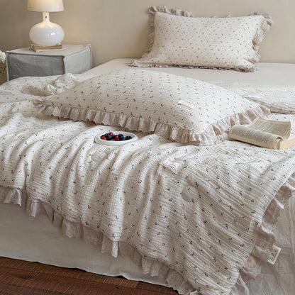 Vintage cottagecore blueberry print comforter with khaki ruffle lace trim, styled with an open book and a small dish of berries on a cozy bed for a French country bedroom aesthetic.