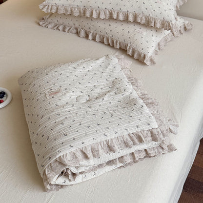 Neatly folded blueberry print gauze comforter showing thick layers of beige scallop lace ruffles, styled with matching country style decorative pillows.
