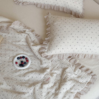 Top-down detailed view of a rustic berry plate resting on a textured, romantic blueberry print cotton muslin blanket with delicate ruffled lace styling.