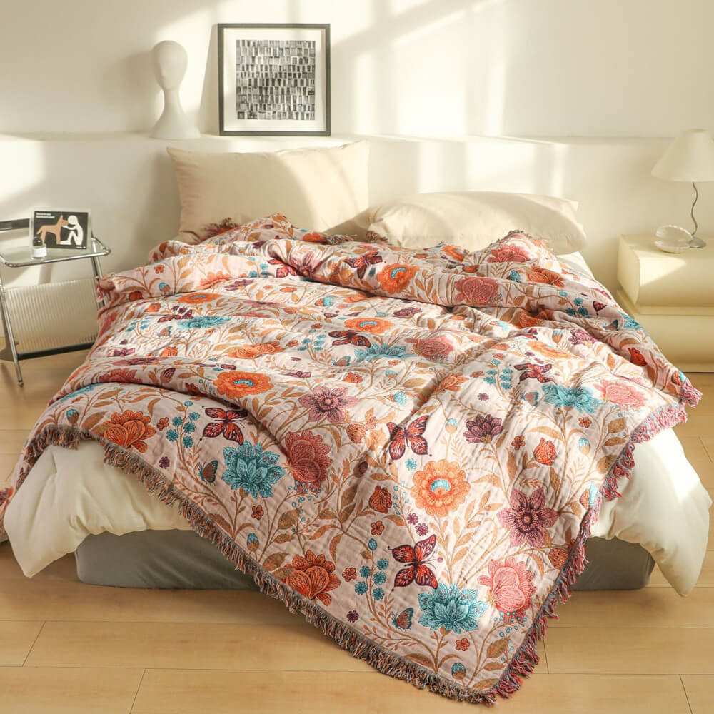 Blush floral cotton throw blanket with fringe styled on a cream bed