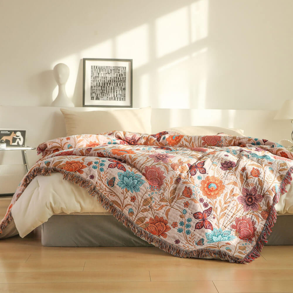 Blush floral cotton throw blanket with coral and teal flowers layered across a bed