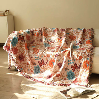 Blush floral cotton throw blanket with fringe draped over a sofa in warm sunlight