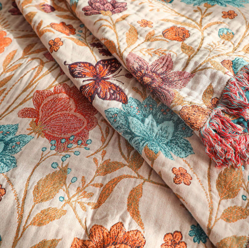 Close-up of blush floral cotton throw blanket with teal flowers and butterfly details