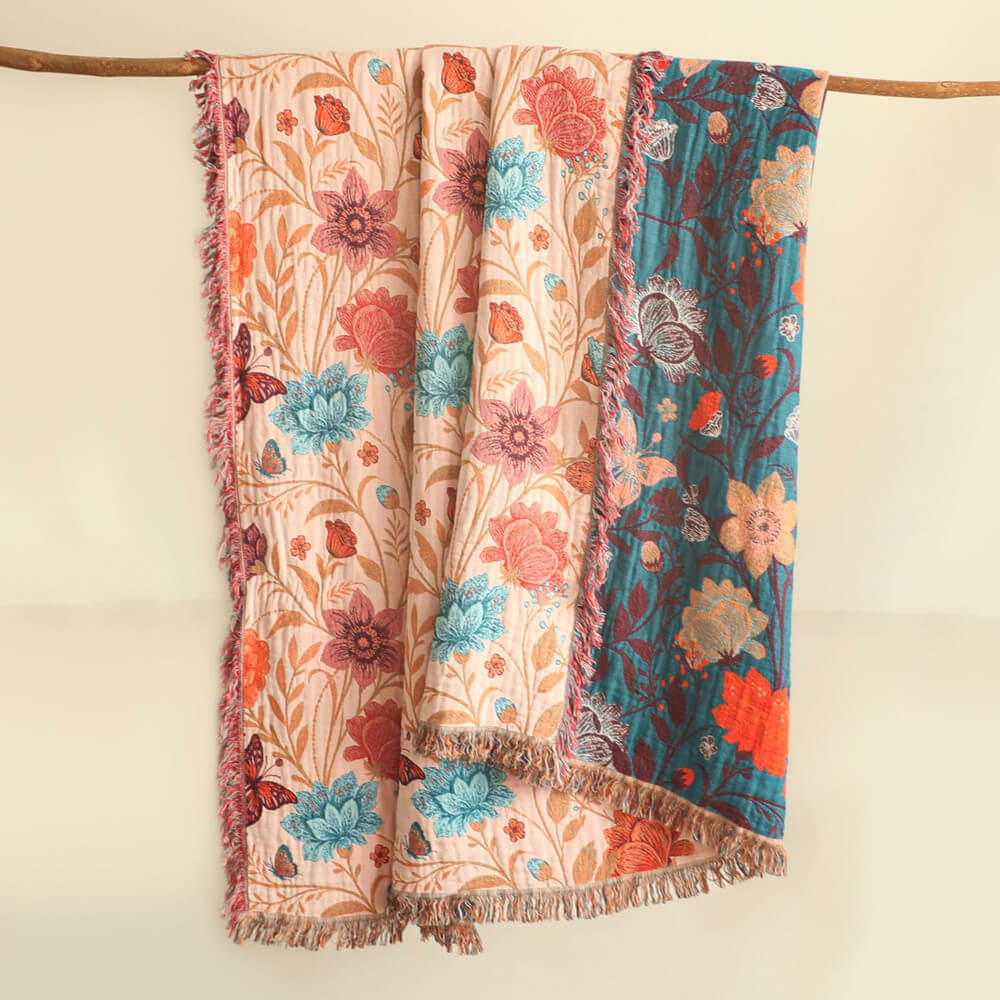 Blush floral cotton throw blanket hanging on a wooden rod with teal reverse side and fringe